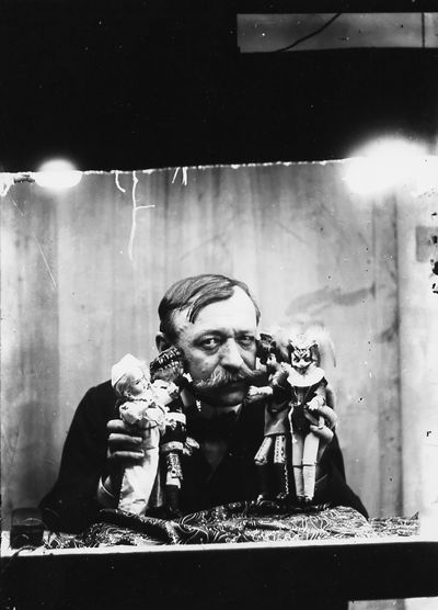 Émile Cohl, le regard vers l'objectif, tenant quatre de ses marionnettes toutes en costume.