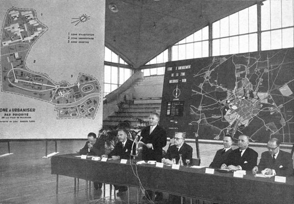 Fig. 8. Photographie de l’ouverture des Journées textiles de Mulhouse en 1961. Au centre, debout, le maire le Muller ; au fond et sur le côté, les plans à différentes échelles du développement de la ville et de l’Université (BSIM, 704, 1961-3, p. 3).