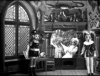 Marguerite assise dans le fond, Faust et Méphistophélès debout en premier plan, dans un décor médieval.